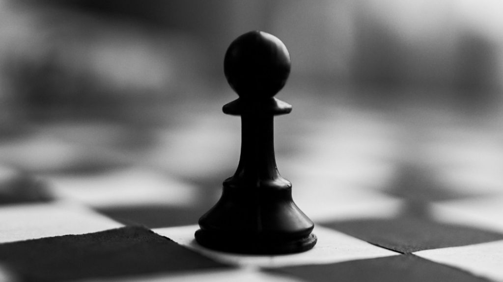 A single black pawn standing alone on a chessboard.